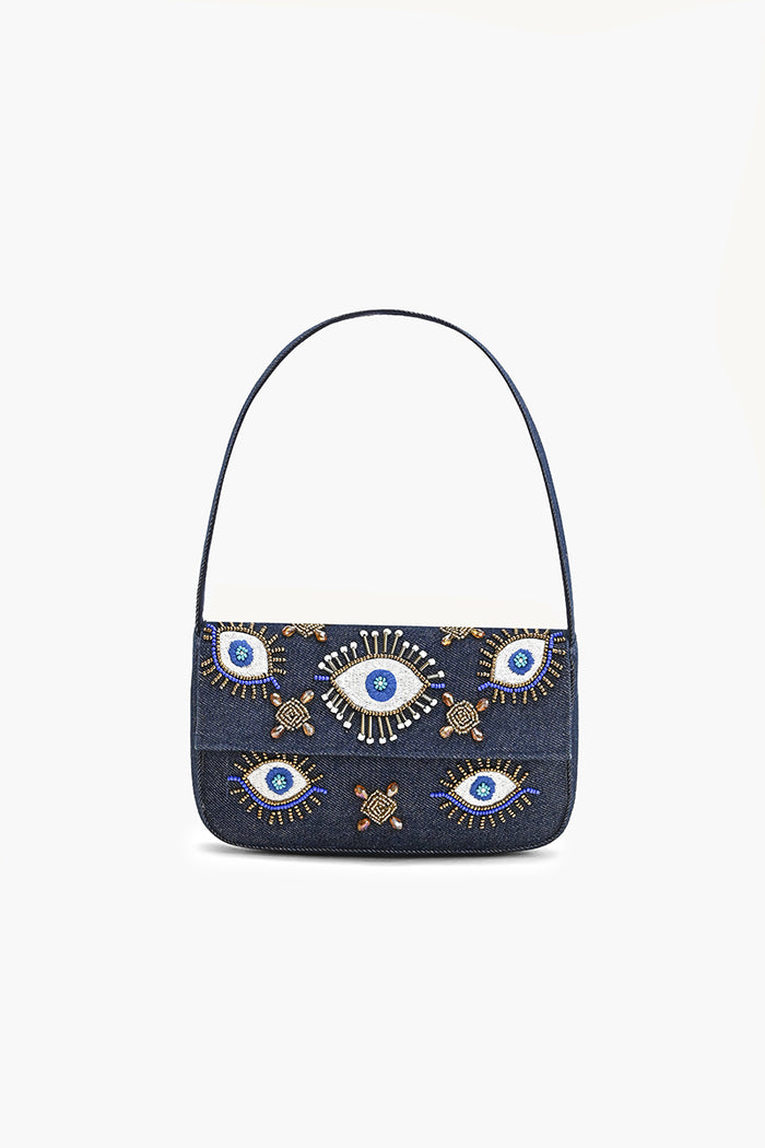 A dark blue denim shoulder bag featuring embroidered evil eye motifs in blue, white, and gold on the front flap, with a single dark blue shoulder strap, shown against a plain white background.